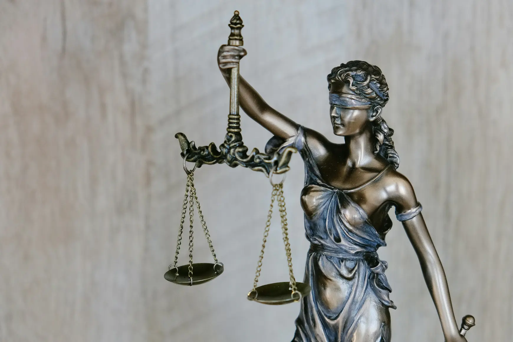 A bronze statue of Lady Justice, blindfolded and holding scales, against a pale wooden background representing the Veilguard bureacracy and passion for justice